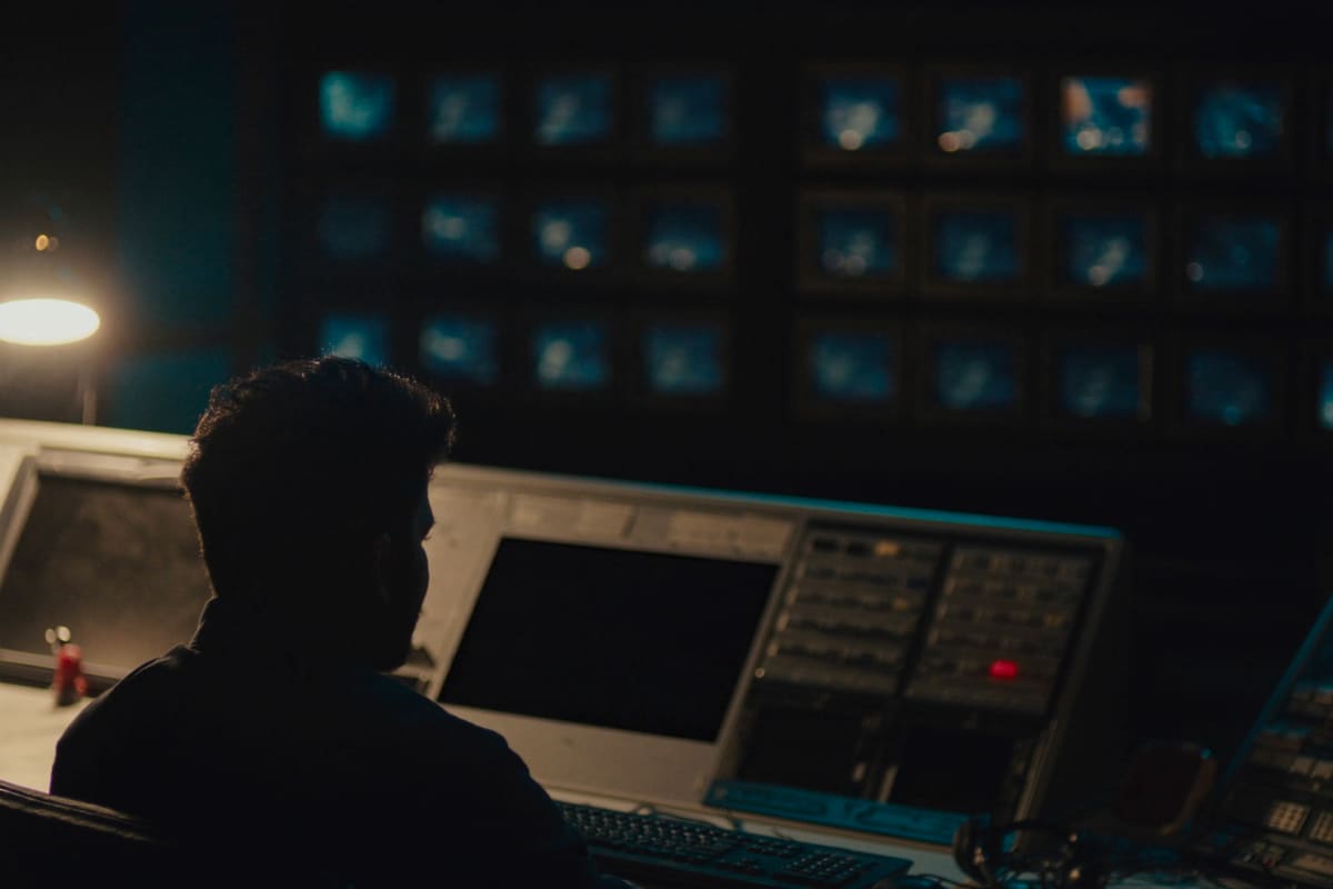 Sala de control de noticias en penumbra, con un operador de espaldas frente a la pared de monitores
